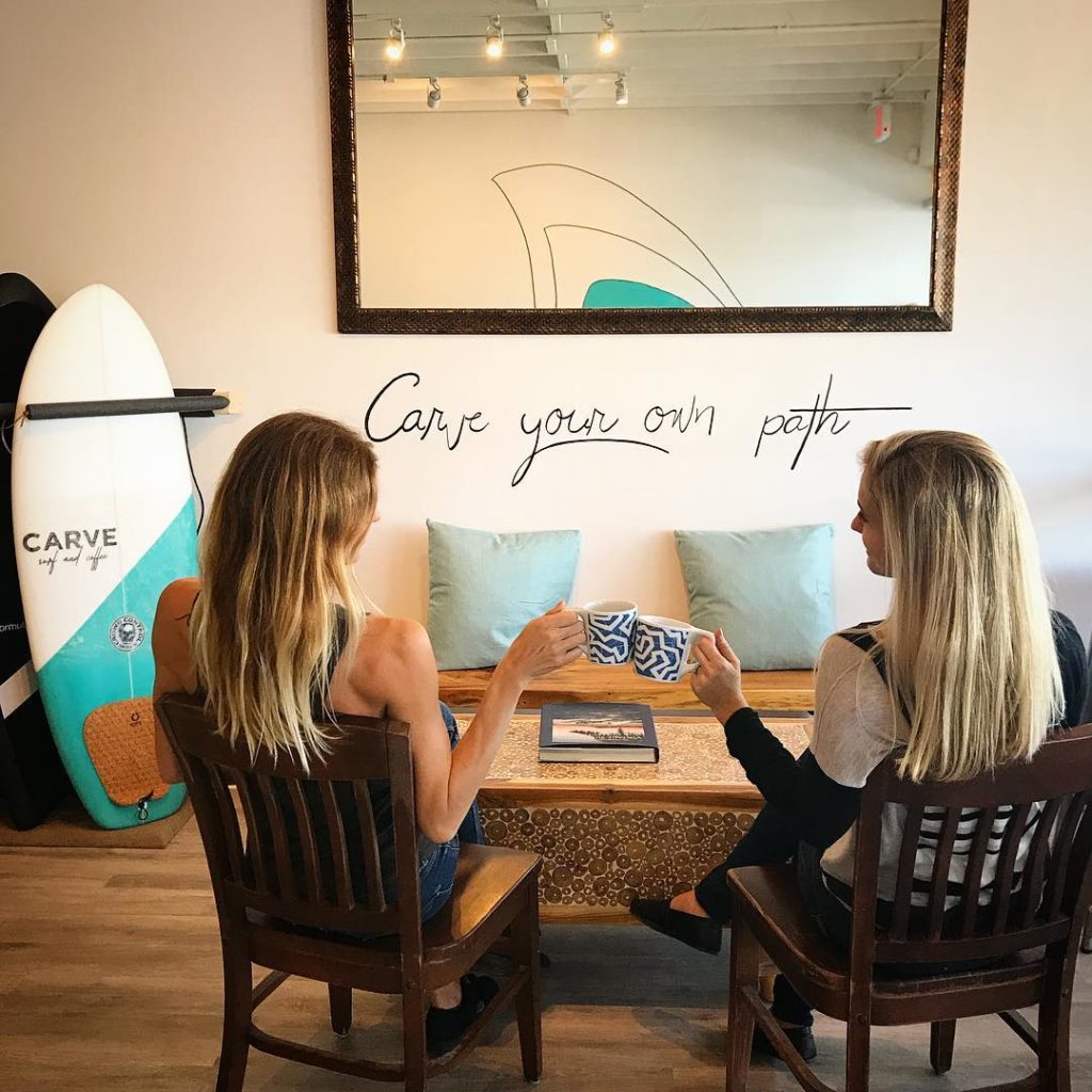Cate and Kim drinking coffee in carve next to a sign, "carve your own path"