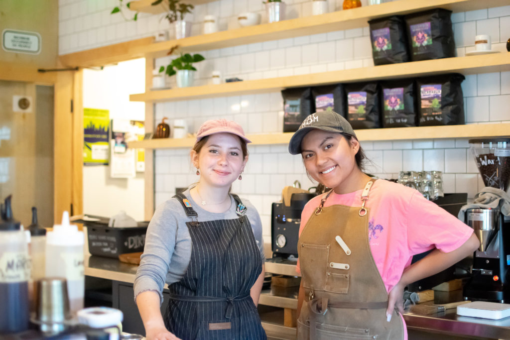 two women, baristas, at coffee shop smiling at camera