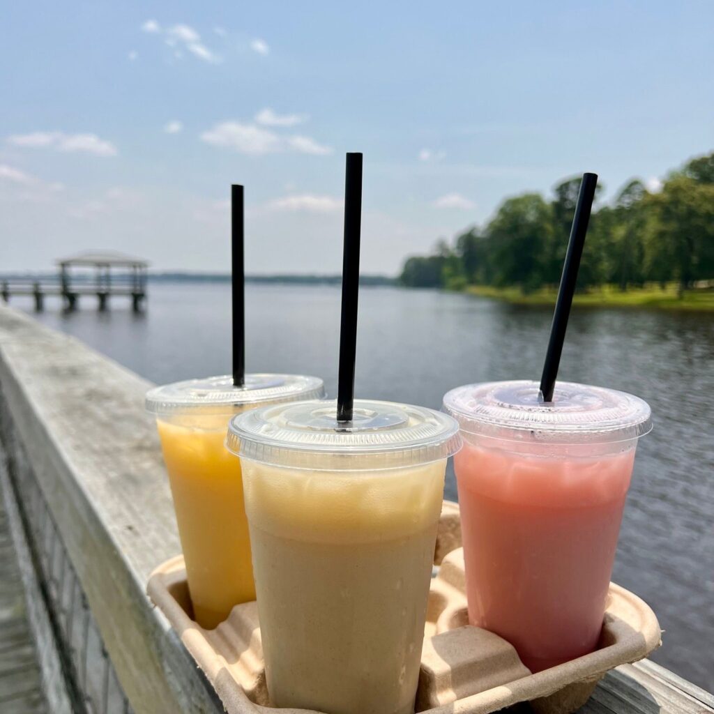Three iced drinks with straws by a lake.