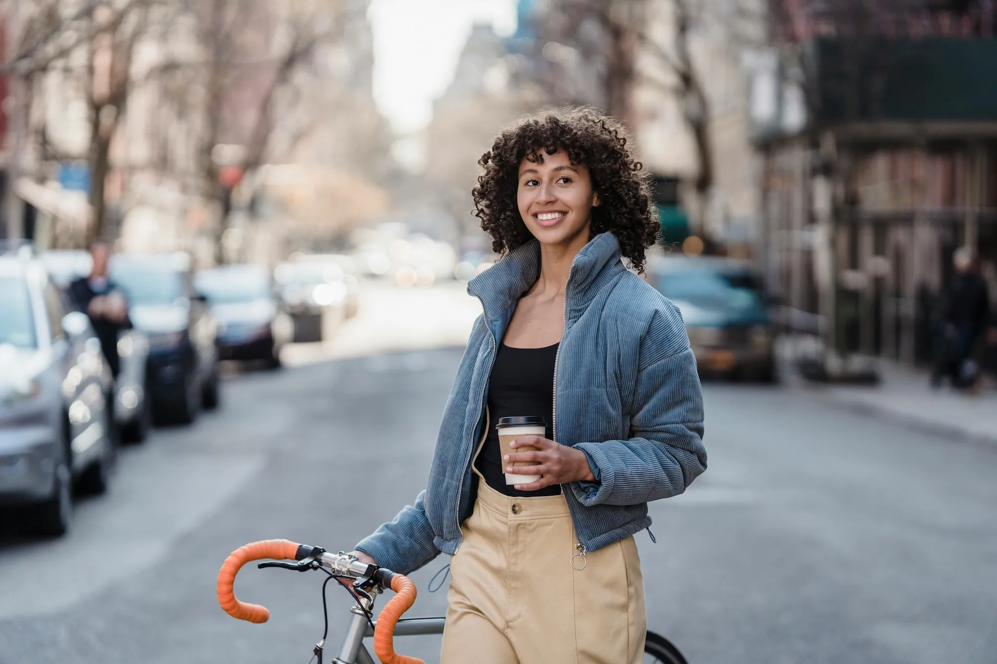 A young person holds a bike and a coffee.